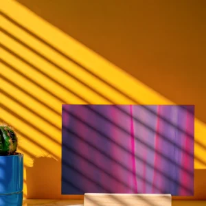 A mini unframed abstract fine art print, propped on a small wooden stand against a yellow wall. Sunlight casts a striped shadow across the artwork and the wall